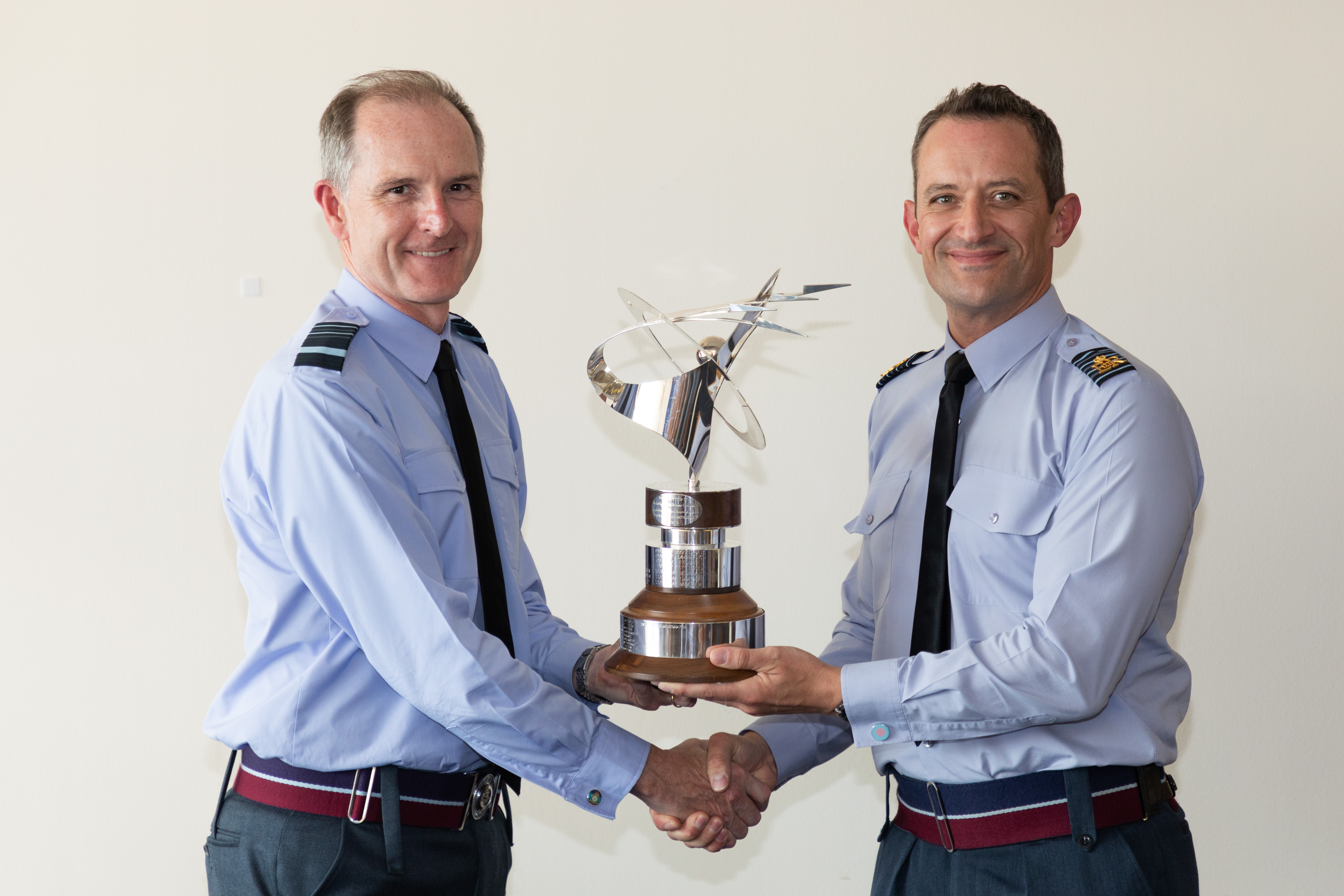 Image shows RAF aviators shaking hands while holding trophy.